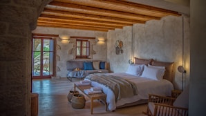 A bedroom with a large bed, wooden beams, stone walls, and a view through a glass door. - Brazzo di Maina (East Mani)