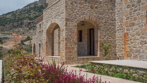 A stone building with arched windows and a balcony, surrounded by a garden with pink flowers. - Brazzo di Maina (East Mani)