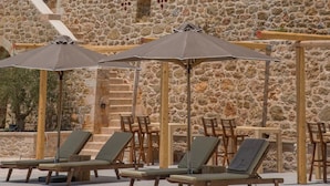 A stone building with a terrace, lounge chairs, and umbrellas. - Brazzo di Maina (East Mani)