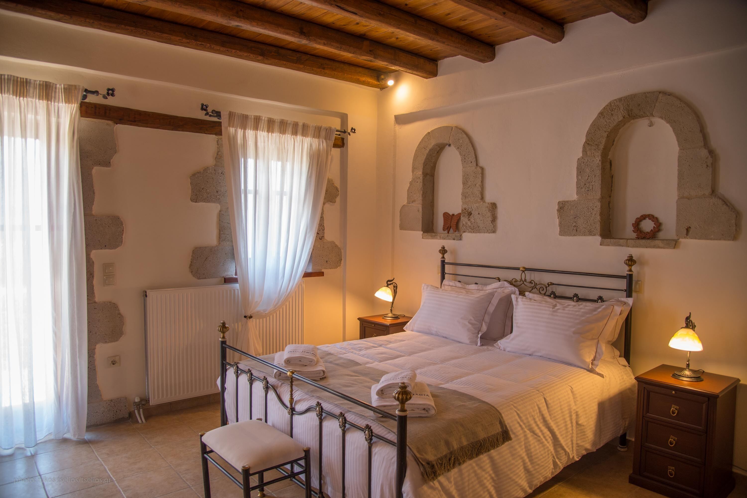A bedroom with a bed, two bedside tables, a nightstand, a chair, and a window with curtains.