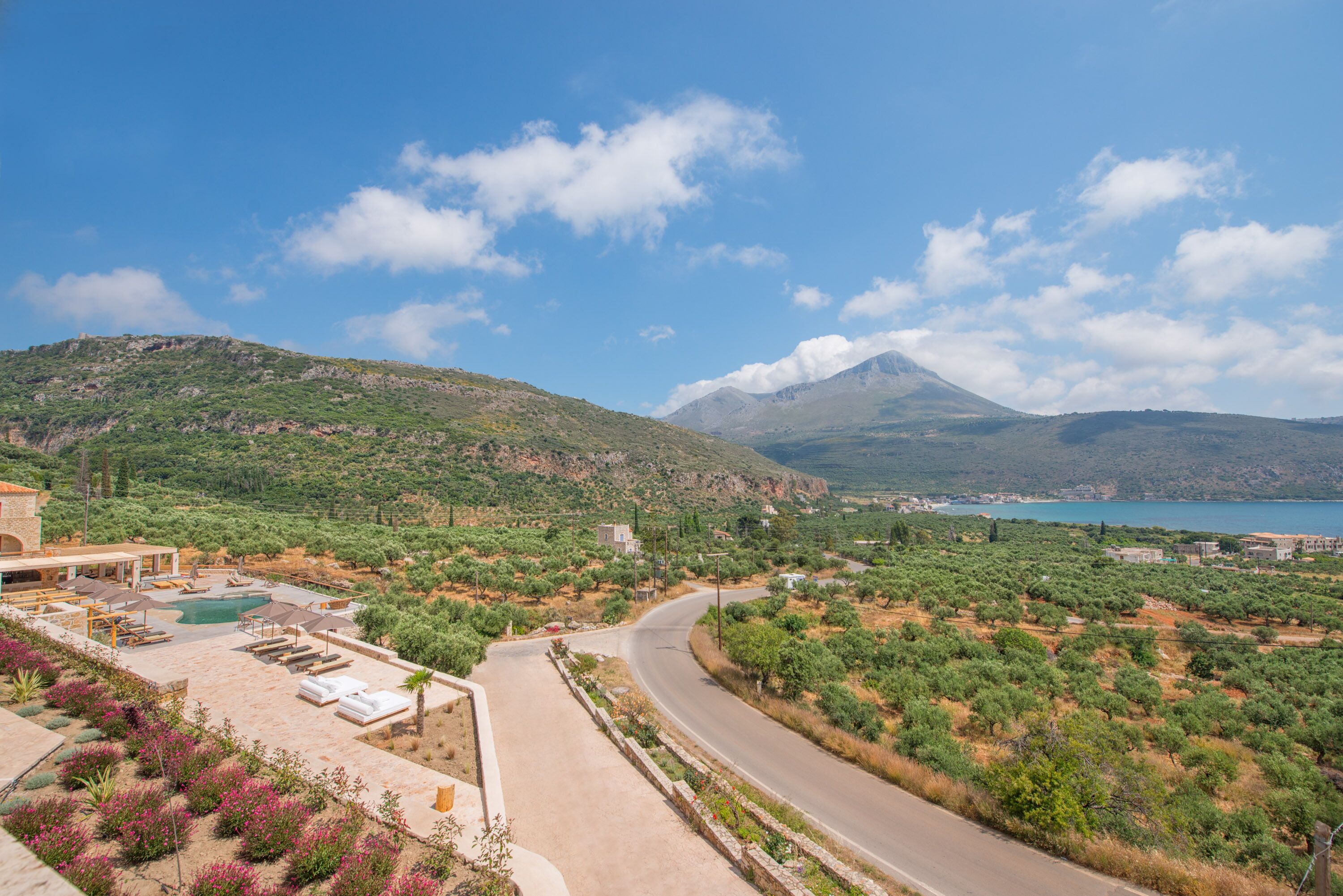 A coastal property with a swimming pool, lounge area, and a view of the sea and mountains.