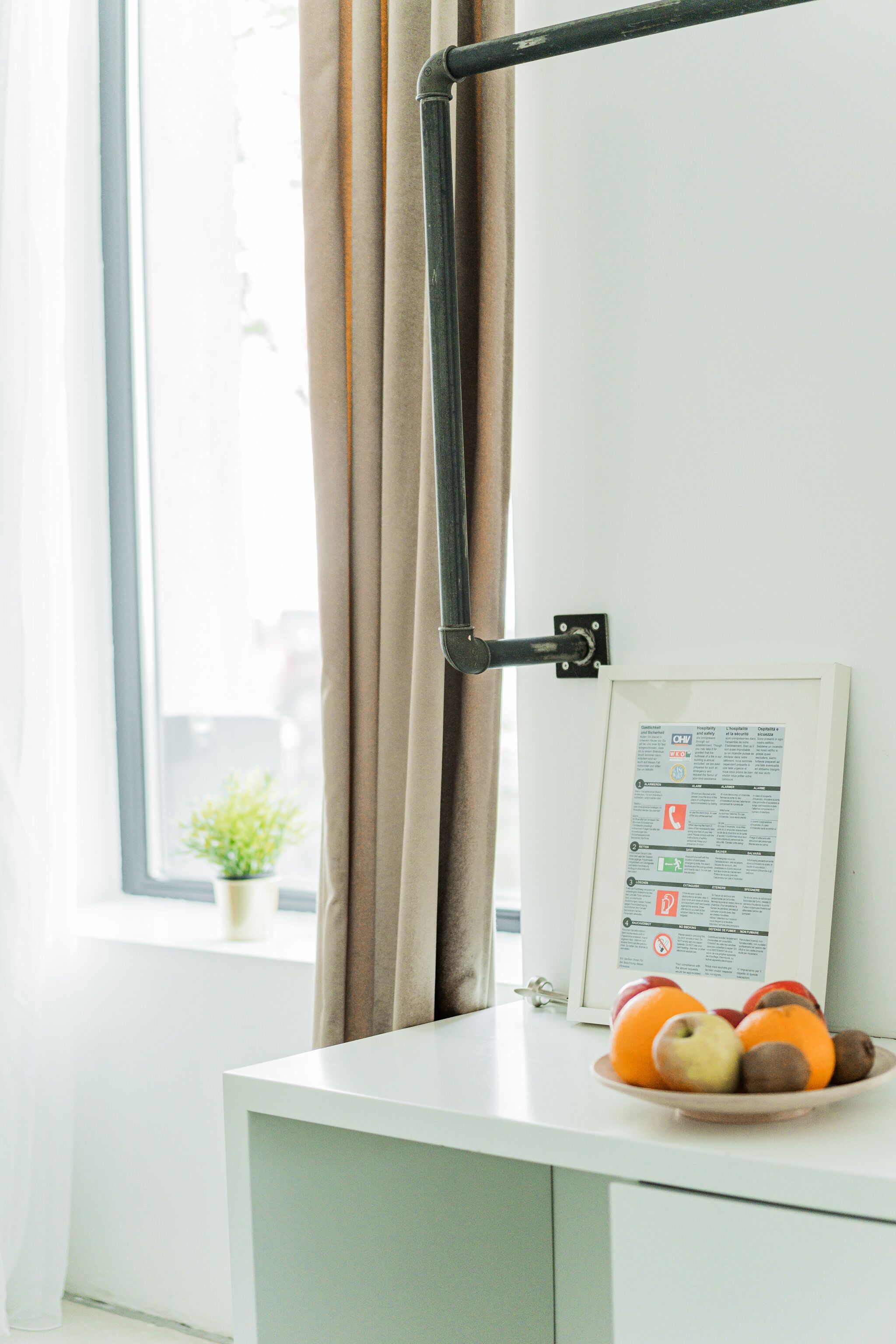 A window with curtains, a small plant, and a framed sign on a white desk.