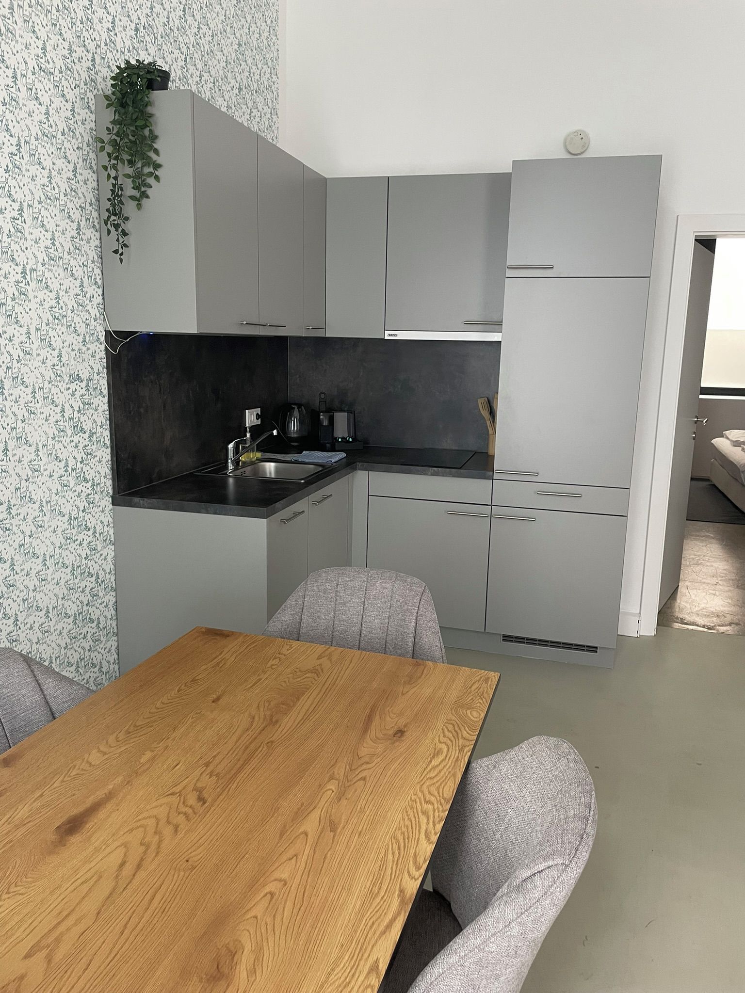 A modern kitchen with grey cabinets, a black countertop, and a wooden dining table.
