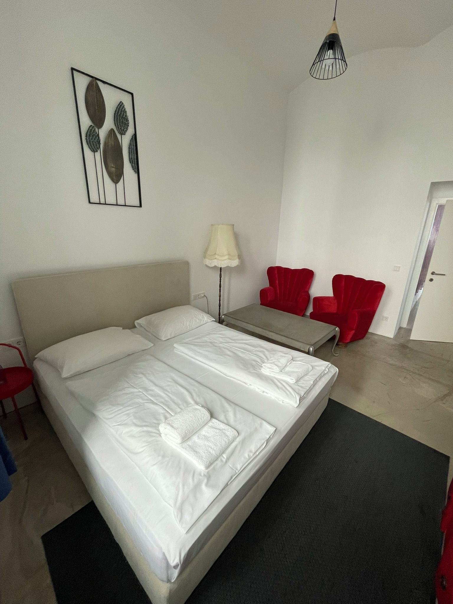 A hotel room with a bed, a bedside table, a lamp, and two red chairs.