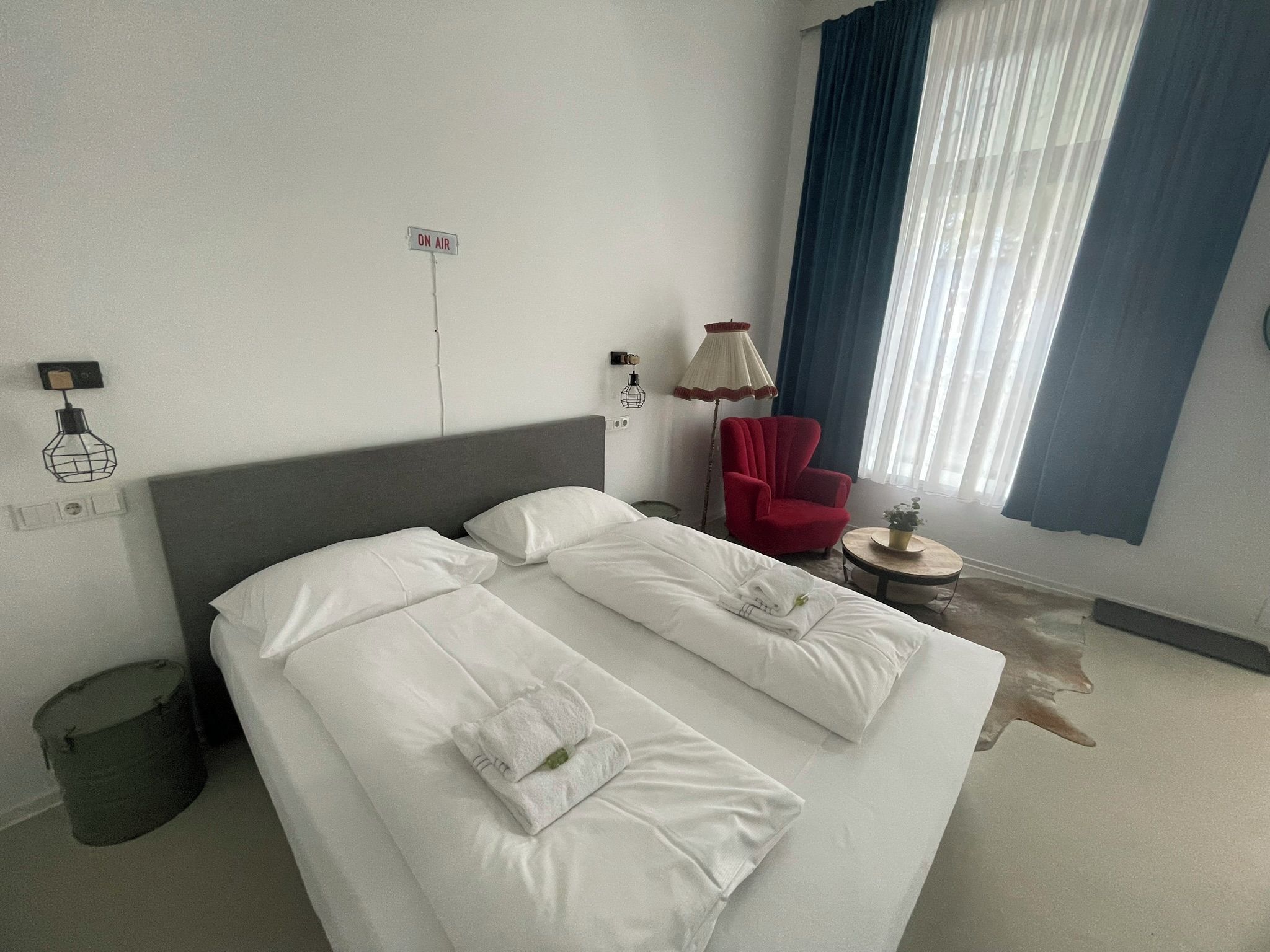 Ein Hotelzimmer mit einem Bett, einem roten Sessel, einer Lampe und einem Fenster mit Vorhängen.