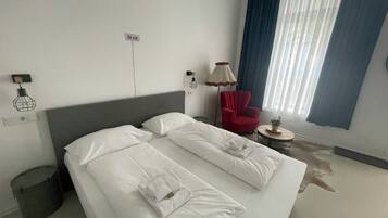 Ein Hotelzimmer mit einem Bett, einem roten Sessel, einer Lampe und einem Fenster mit Vorhängen.