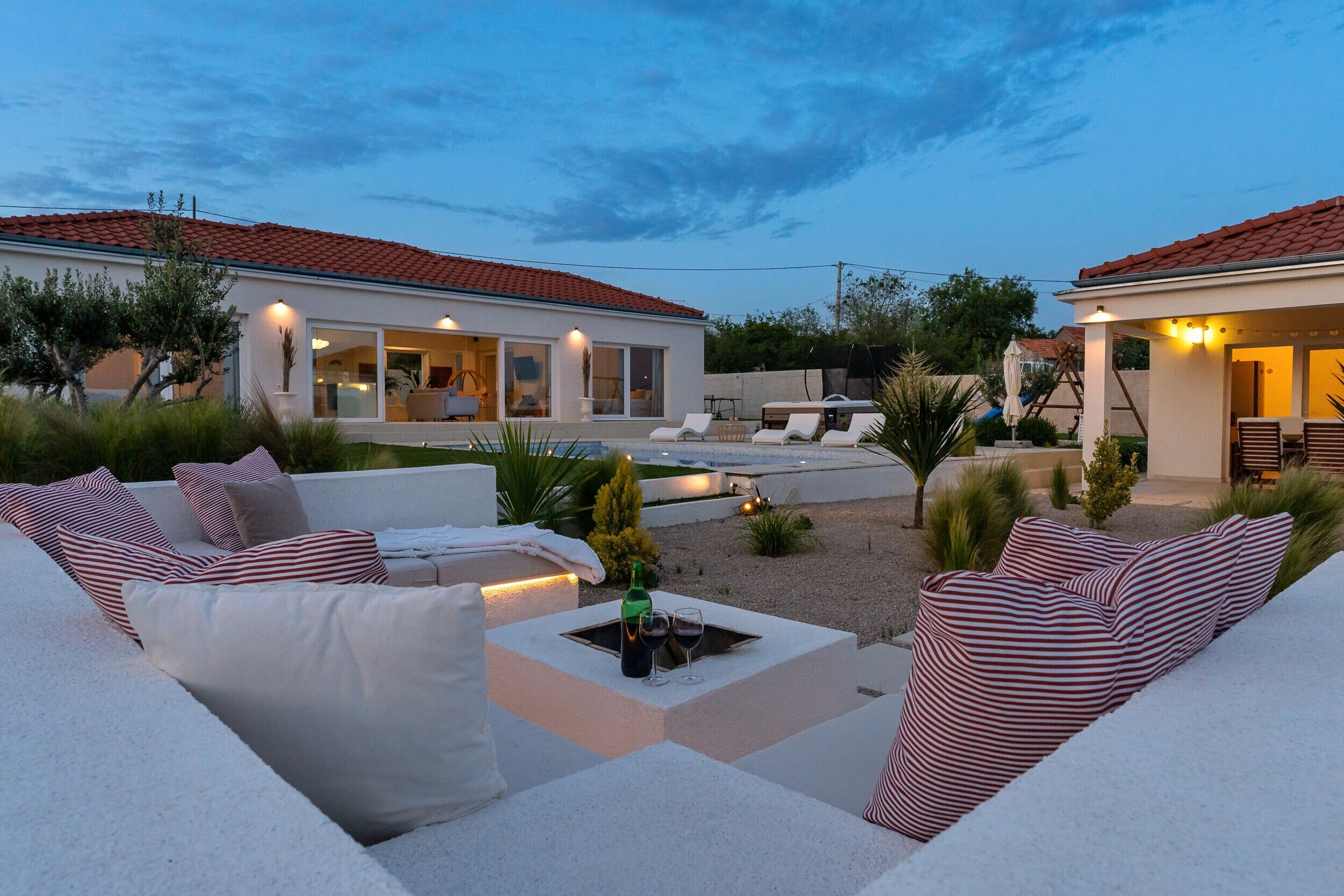 Un área exterior moderna con piscina, sillas de descanso y un patio bien iluminado.