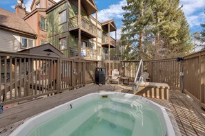 Une terrasse en bois avec un jacuzzi, une clôture en bois et un bâtiment à deux étages doté de balcons.