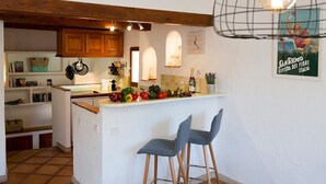 A kitchen with wooden cabinets, a white countertop, and two bar stools. There is a clock on the wall and a poster on the wall. - Bright and large apartment in heart of the old town (Antibes)