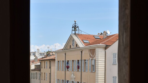 A view from a balcony with terracotta roof tiles, overlooking a street with buildings featuring traditional architecture, including a building with a sign that reads "Galerie Clémence." - Bright and large apartment in heart of the old town (Antibes)