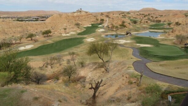 Un parcours de golf avec un chemin sinueux, des obstacles d’eau et une végétation clairsemée.