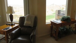 Une pièce comprenant un fauteuil en cuir, une lampe, une petite table et donnant sur un terrain de golf grâce à de grandes fenêtres.