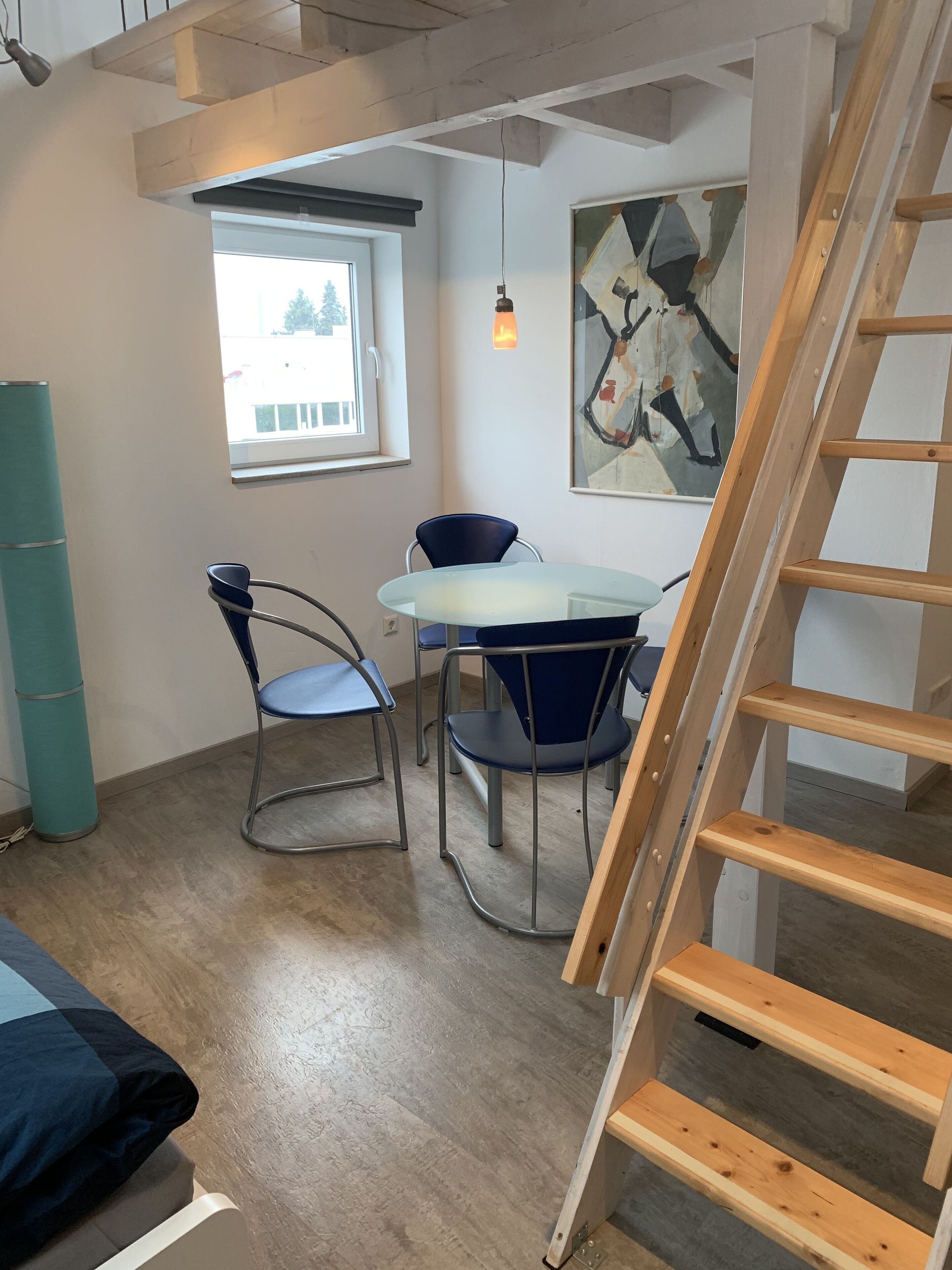 Comedor con una mesa redonda, dos sillas, un cuadro en la pared y una escalera de madera.