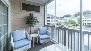 A balcony with wicker chairs, a small table, and a 'BEACH' sign on the wall. - Beautiful Golf Villa, 2.7 Miles To Beach + Free Attraction Tickets! (North Myrtle Beach)