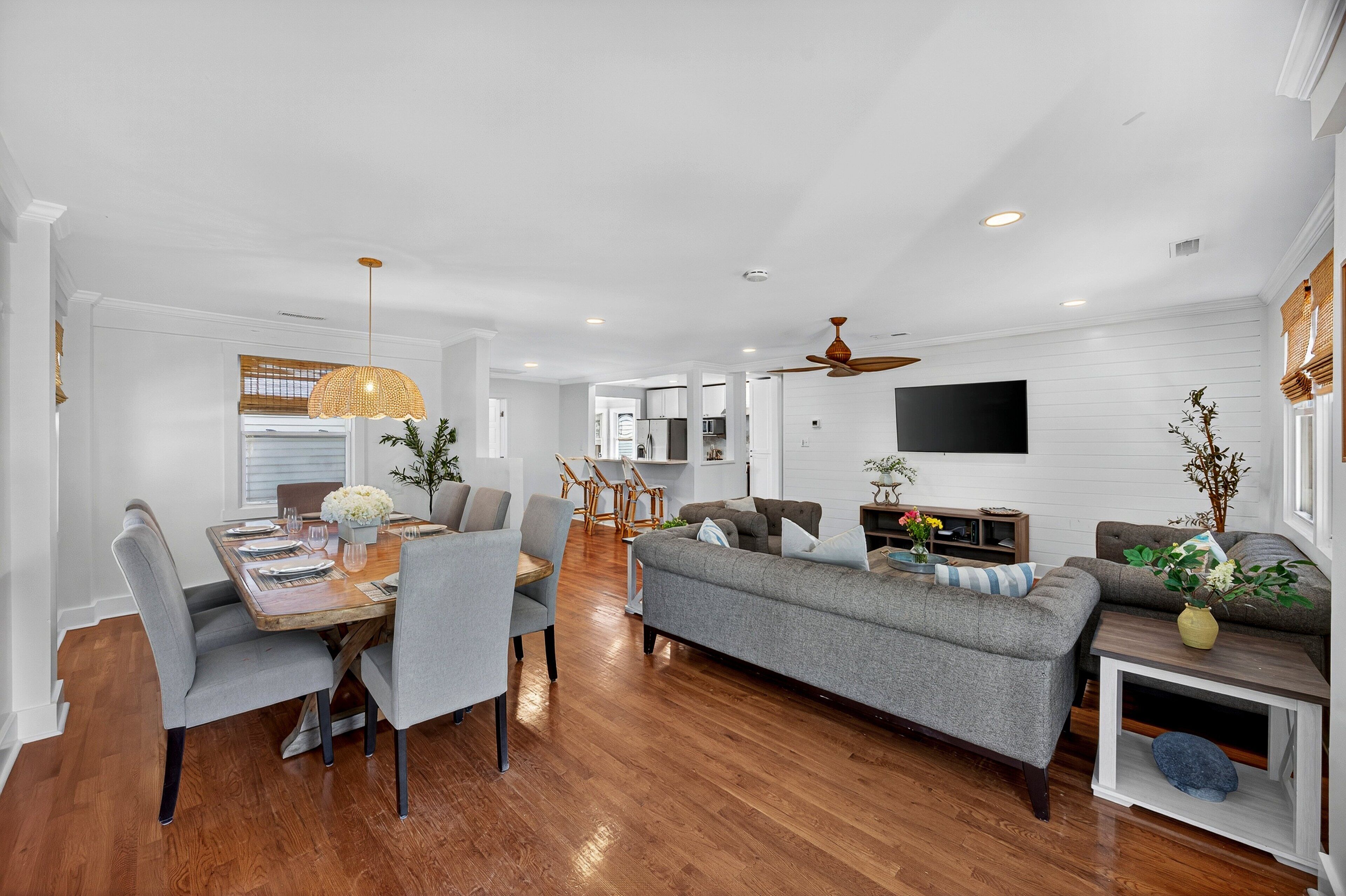 A spacious living room with a dining area, wooden flooring, and a ceiling fan.