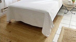 Une chambre à coucher comprenant un lit, un ventilateur de plafond, un climatiseur mural, une lampe de chevet, un tableau encadré et une petite table avec une plante.
