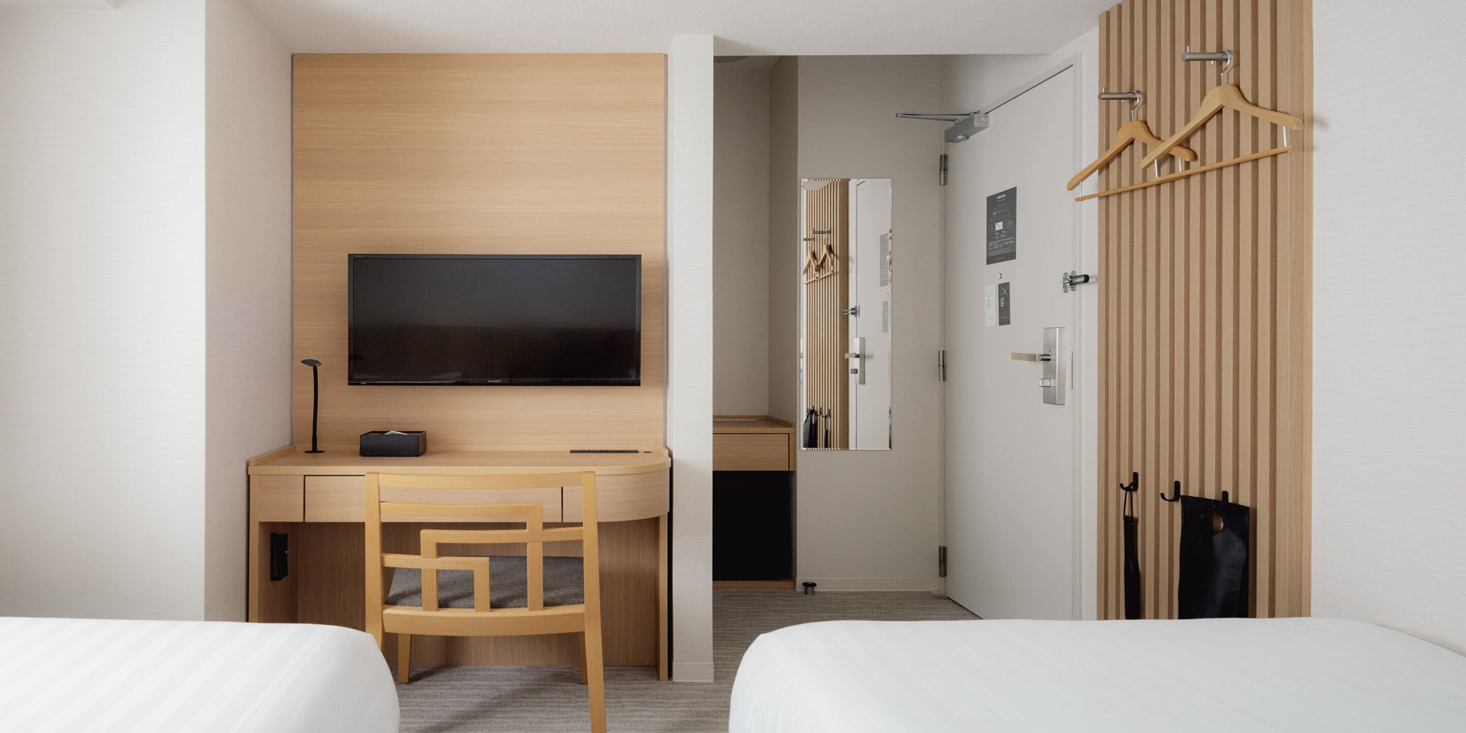 Ein Hotelzimmer mit einem Bett, einem Schreibtisch mit Fernseher, einem Sessel und einem Kleiderschrank mit Kleiderbügeln.