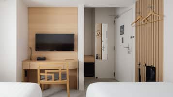 Ein Hotelzimmer mit einem Bett, einem Schreibtisch mit Fernseher, einem Sessel und einem Kleiderschrank mit Kleiderbügeln.