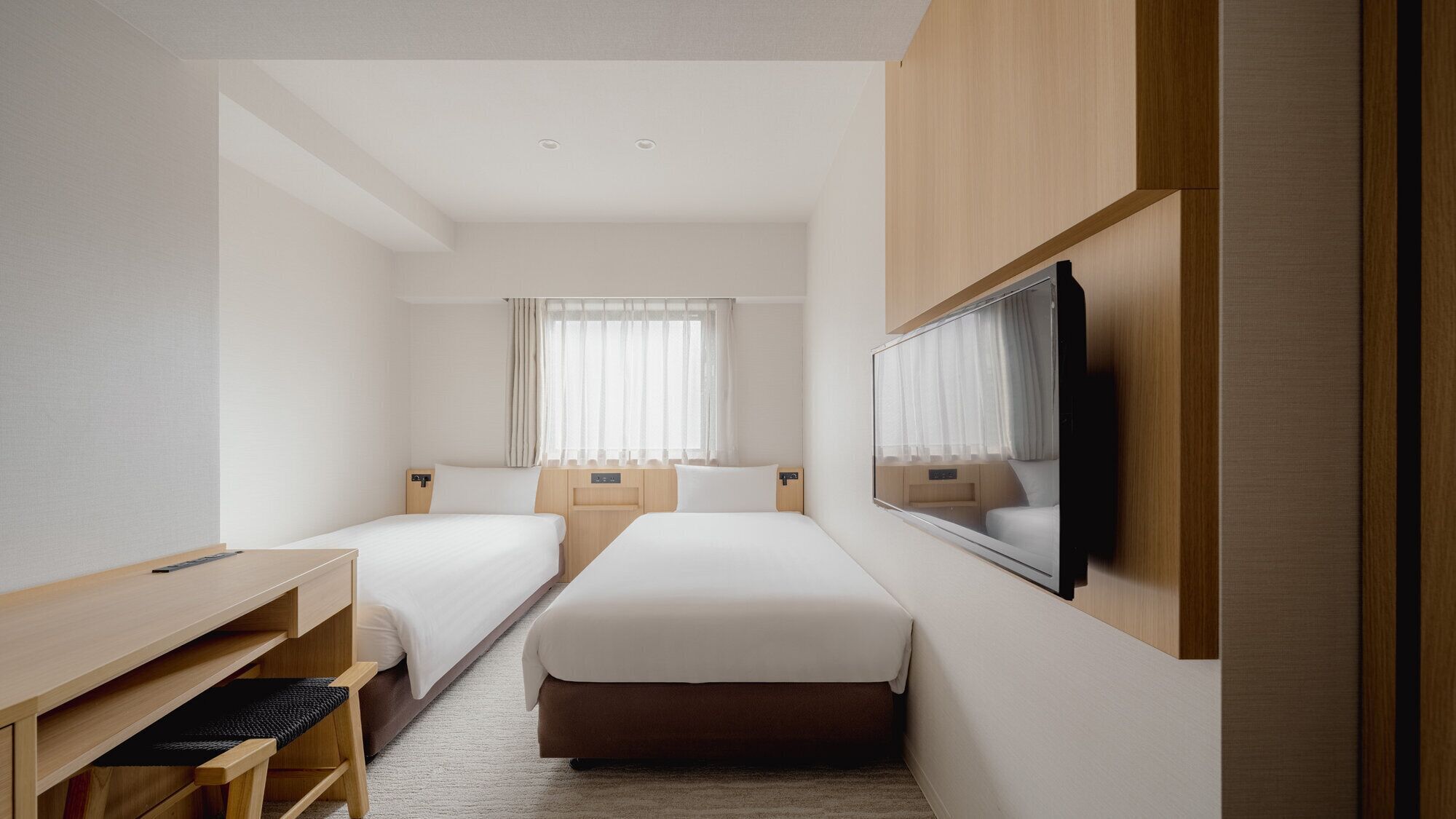 A hotel room with two beds, a desk, a TV, and a window with curtains.