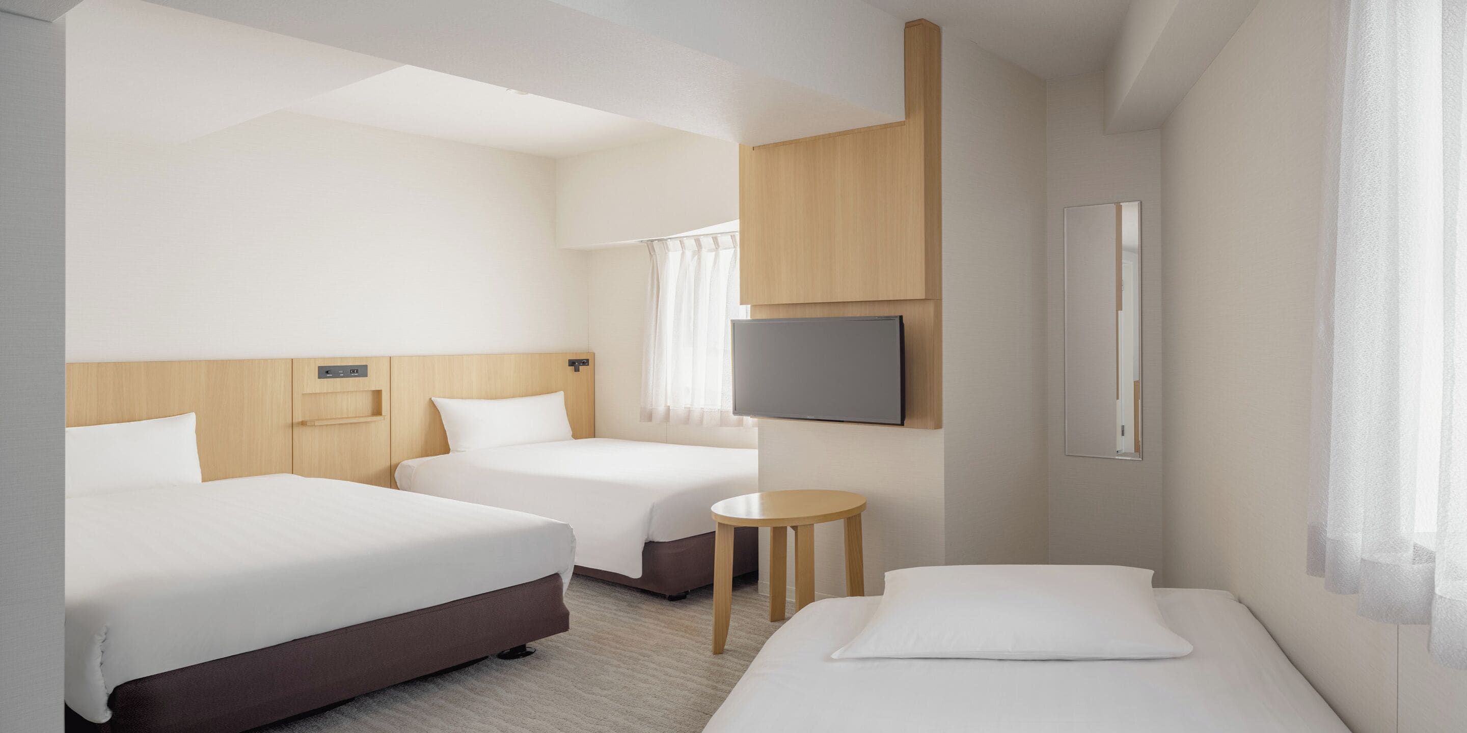 Een hotelkamer met twee bedden, een televisie, een tafeltje en een raam met gordijnen.