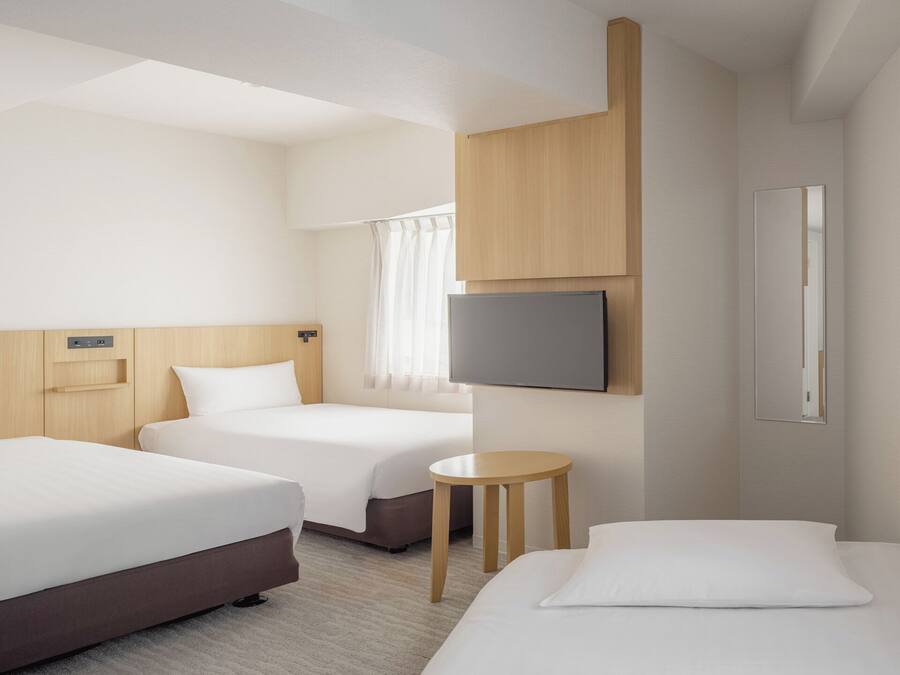 Een hotelkamer met twee bedden, een televisie, een tafeltje en een raam met gordijnen.