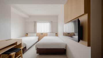 A hotel room with two single beds, a desk, a television, and a window with curtains.