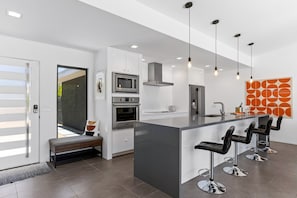 A modern kitchen with a central island, bar stools, and pendant lighting.