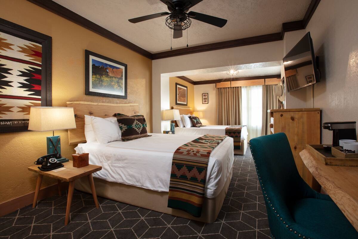 A hotel room with a bed, a desk with a telephone, a chair, a television, and a ceiling fan.
