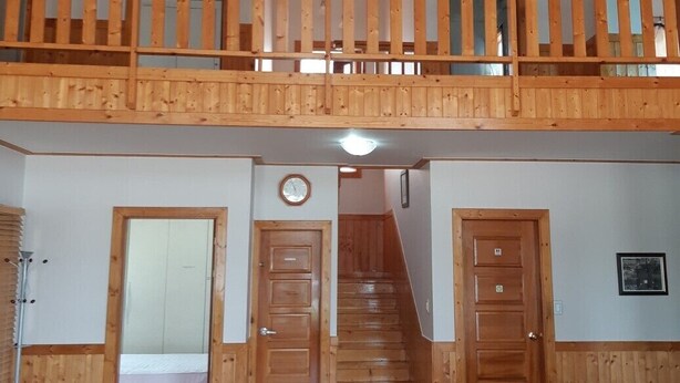A spacious loft bedroom with a wooden balcony, a staircase, and a large bed. - Marina Pension (Ansan)