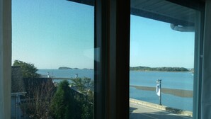A view through a window with a clear sky, a body of water, and a distant shoreline. - Marina Pension (Ansan)