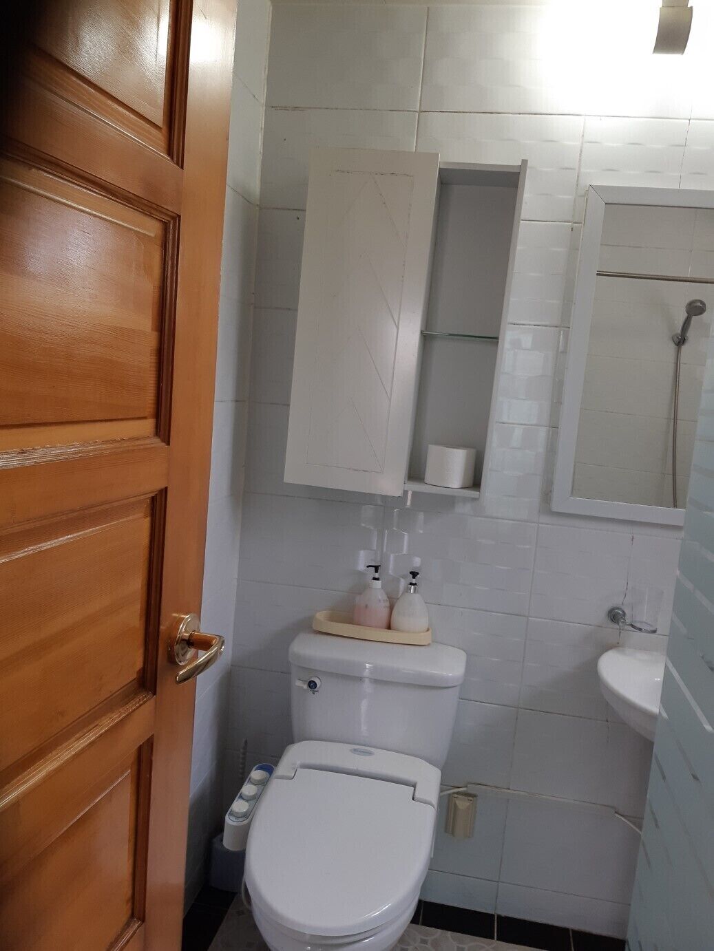 A bathroom with a wooden door, white toilet, and a sink with a mirror above it.