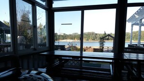 A view from a covered deck with a wooden floor, large windows, and a view of a lake and trees. - Marina Pension (Ansan)