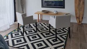 Ein modernes Wohnzimmer mit großem Fenster, einer hängenden Gewebedeckenleuchte, einem Holzsurfbrett und einem Essbereich mit zwei Stühlen und einem Tisch.