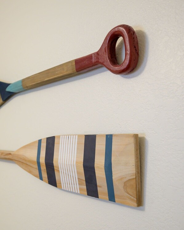 Dos herramientas de madera, una con mango rojo y la otra con diseño a rayas, sobre un pared lisa.