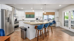 A modern kitchen with white cabinets, stainless steel appliances, and a central island with bar stools. - Large Pool and Entertainers Delight Yard! (Phoenix)