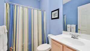 Une salle de bain avec un rideau de douche à rayures, des toilettes blanches, un lavabo avec un miroir et un tableau encadré au mur.
