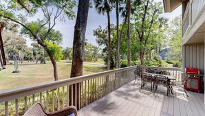 A wooden deck with outdoor furniture, overlooking a grassy area with trees and a golf course in the background. - Large Three Bedroom Villa Directly on George Fazio Championship Golf Course! (Hilton Head)