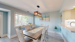 A dining area with a wooden table, white chairs, and a patterned table runner. There is a window with a view of trees and a ceiling light fixture. - Large Three Bedroom Villa Directly on George Fazio Championship Golf Course! (Hilton Head)