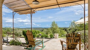 Een terras met schommelstoelen, een tafel en uitzicht op een groen landschap.