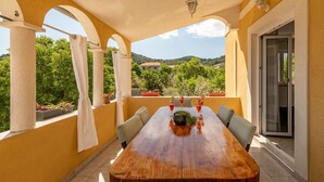 Una mesa de comedor de madera con sillas, una planta en maceta y vistas a zonas verdes y colinas.