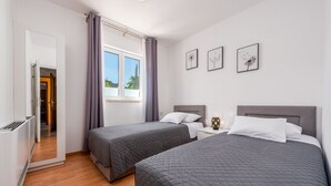 Habitación de hotel con dos camas, una ventana con cortinas, un radiador y tres cuadros colgados en la pared.