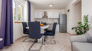 Cocina compacta con mesa, sillas, refrigerador y una planta en maceta.