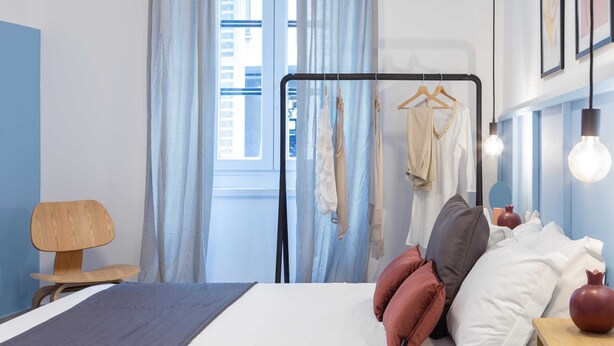 Quarto de hotel moderno com cama, cabideiro e janela com cortinas.