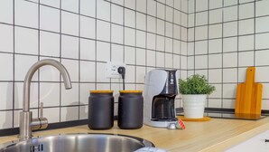 Uma cozinha moderna com pia de aço inoxidável, cafeteira, dois potes, uma planta em vaso e tábua de corte de madeira.