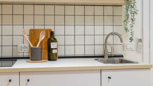 Eine Küche mit weißer Arbeitsplatte, einer Edelstahl-Spüle, einem Holzer Schneidebrett, einer Olivenölflasche und einer Pflanze an der Wand.