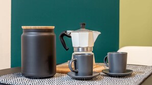 En kaffestation med en mörk kaffekanna, en vit och svart kaffebryggare och två matchande koppar på ett bricka med mönster.