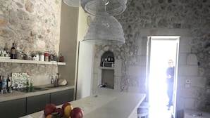 A kitchen with a stone wall, a fruit bowl on the counter, and a person standing in the doorway. - Townhome (Castrignano De' Greci)