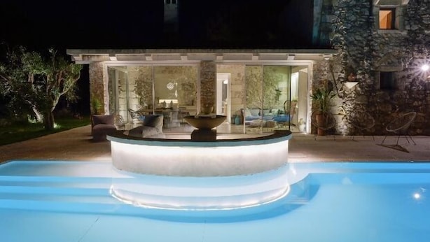 A swimming pool with a built-in fountain, surrounded by a stone wall and a well-lit outdoor seating area. - Townhome (Castrignano De' Greci)
