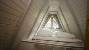 A triangular attic bedroom with a bed, a window, and a sloped ceiling.