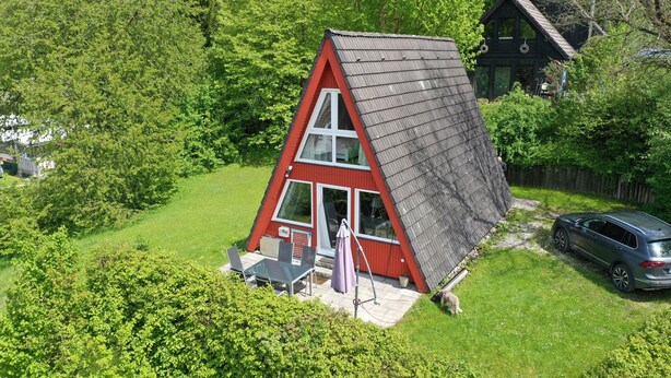 A red and white house with a slanted roof, surrounded by lush greenery.